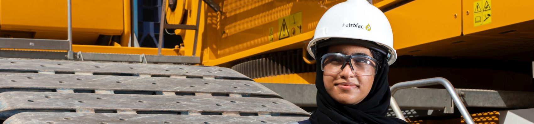 Female Emirati engineeer standing on a project site in full PPE with a white hard hat boasting Petrofac's logo