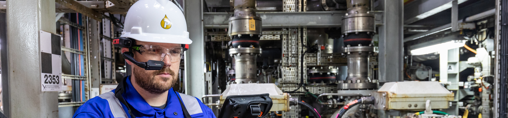 Offshore worker with a white Petrofac hard hat on and a digital device attached to his ear 