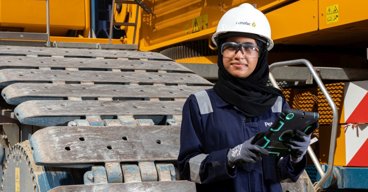 Female Emirati engineeer standing on a project site with in full PPE with a white hard hat boasting Petrofac's logo